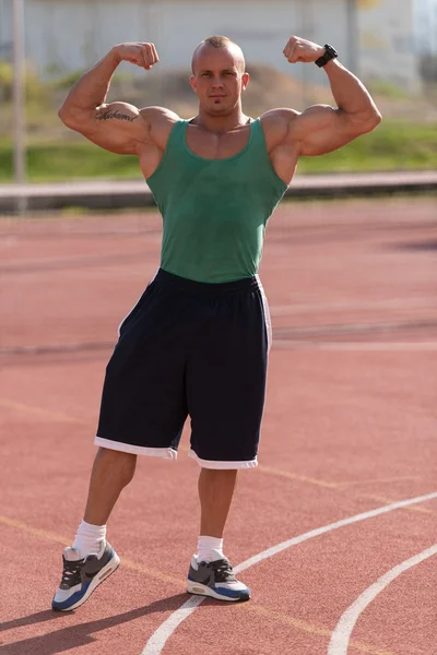 Bodybuilder uitvoeren voorzijde dubbele biceps op tennis plaats — Stockfoto