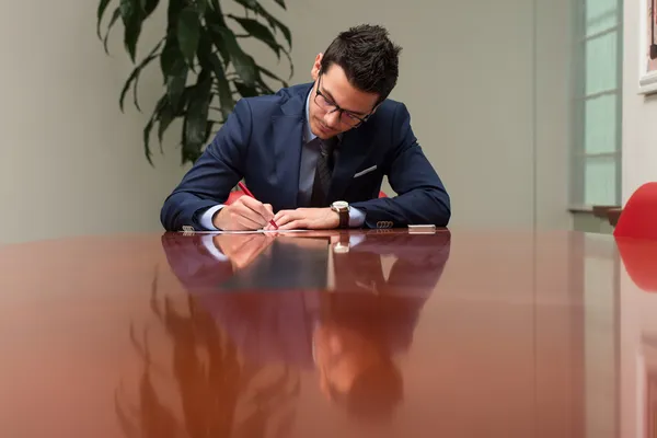 Hombre de negocios sentado en el escritorio de la oficina firmando un contrato —  Fotos de Stock