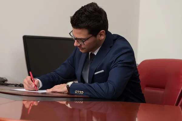 Hombre de negocios sentado en el escritorio de la oficina firmando un contrato —  Fotos de Stock