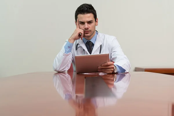 Ylityöllistetty lääkäri istuu pöytänsä ääressä — kuvapankkivalokuva