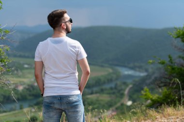 Genç ve mutlu bir adamın portresi. Dağın tepesinde dikiliyor. Kameraya doğru.