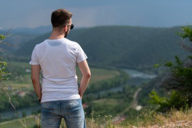 Genç ve mutlu bir adamın portresi. Dağın tepesinde dikiliyor. Kameraya doğru.