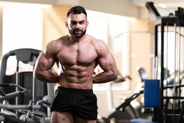Yakışıklı Genç Adam Spor Salonunda Güçlü Duruyor ve Kaslarını Geriyor - Kas Atletik Vücut Geliştirici Spor Sonrası Spor Pozisyonu
