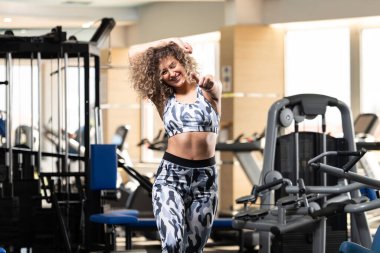 Spor salonunda güçlü bir şekilde ayakta duran ve kaslarını esneten Sağlıklı Genç Kadın Egzersiz yaptıktan sonra güzel bir spor mankeni pozu veriyor