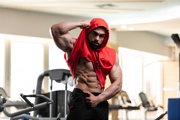 Young Man Standing Strong In The Gym And Flexing Muscles in a Red Hoodie  - Muscular Athletic Bodybuilder Fitness Model Posing After Exercises