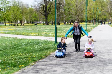 Anne ve Çocuklar Parkta Oyuncak Arabayla Oynuyor - Mutlu Bir Oğlan ve Kız Caddede Mavi ve Kırmızı Oyuncak Arabayla Geziniyor