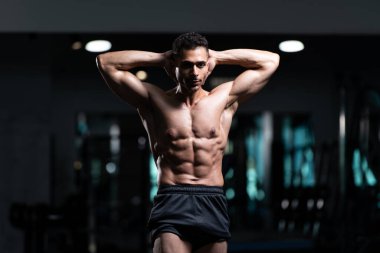 Gynecomastia göğüsleri olan yakışıklı genç adam spor salonunda güçlü duruyor ve kaslarını kasıyor.