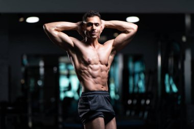 Gynecomastia göğüsleri olan yakışıklı genç adam spor salonunda güçlü duruyor ve kaslarını kasıyor.