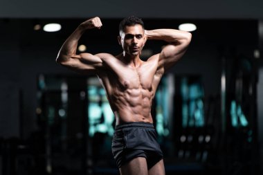 Gynecomastia göğüsleri olan genç adam spor salonunda güçlü duruyor ve kaslarını kasıyor.