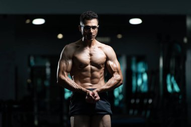 Gynecomastia göğüsleri olan yakışıklı genç adam spor salonunda güçlü duruyor ve kaslarını kasıyor.