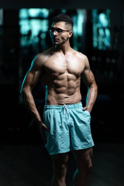 Gynecomastia göğüsleri olan yakışıklı genç adam spor salonunda güçlü duruyor ve kaslarını kasıyor.