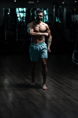 Gynecomastia göğüsleri olan genç adam spor salonunda güçlü duruyor ve kaslarını kasıyor.