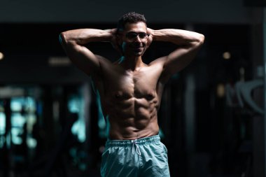 Gynecomastia göğüsleri olan genç adam spor salonunda güçlü duruyor ve kaslarını kasıyor.