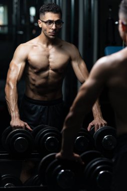 Gynecomastia göğüsleri olan genç adam spor salonunda güçlü duruyor ve kaslarını kasıyor.