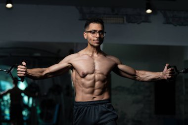 Gynecomastia göğüsleri olan bir adam spor salonunda kablolu TV ile göğüs çalışıyor.