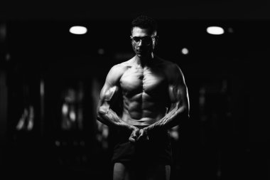 Gynecomastia göğüsleri olan yakışıklı genç adam spor salonunda güçlü duruyor ve kaslarını kasıyor.