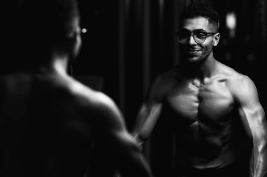 Gynecomastia göğüsleri olan yakışıklı genç adam spor salonunda güçlü duruyor ve kaslarını kasıyor.