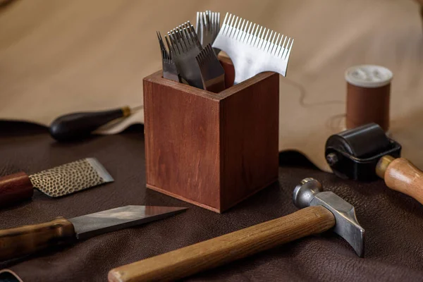 Shoemaker tools for sewing handmade shoes in workshop. Wood box with punches, awl, knives, hammer on beige and brown piece of genuine leather