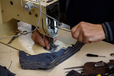 Ayakkabıcı atölyesindeki profesyonel endüstriyel dikiş makinesiyle sorunu tamir eden tamirci elleri. Makine dikişleri test ediliyor. Seçici odak