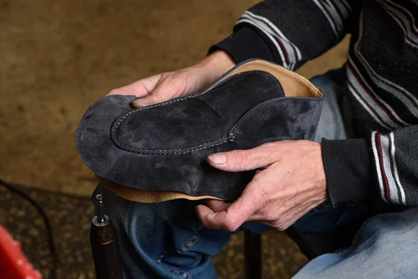 Bootmaker making shoes sitting in workshop. Shoemaker holding gray suede shoe in hands before stitching. Bespoke handmade shoes