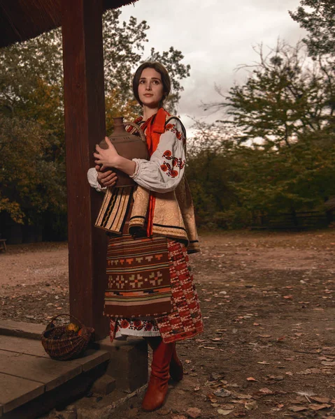 多愁善感的年轻女子穿着传统的乌克兰绣花衣服 手里拿着旧陶器 望着远方 古董店 — 图库照片