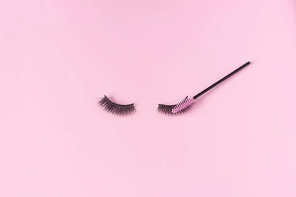 Artificial eyelashes on a pink background and an eyelash brush. The concept of eyelash extensions, makeup.