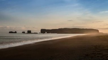 Reynisfjara 'nın kara kumsalındaki keskin kayalıklar sisli yağmurlu bir günde kıyıya vuran dalgalar. Vik, İzlanda.