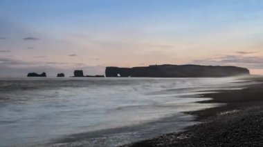Reynisfjara 'nın kara kumsalındaki keskin kayalıklar sisli yağmurlu bir günde kıyıya vuran dalgalar. Vik, İzlanda.