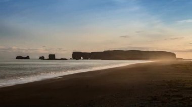 Reynisfjara 'nın kara kumsalındaki keskin kayalıklar sisli yağmurlu bir günde kıyıya vuran dalgalar. Vik, İzlanda.