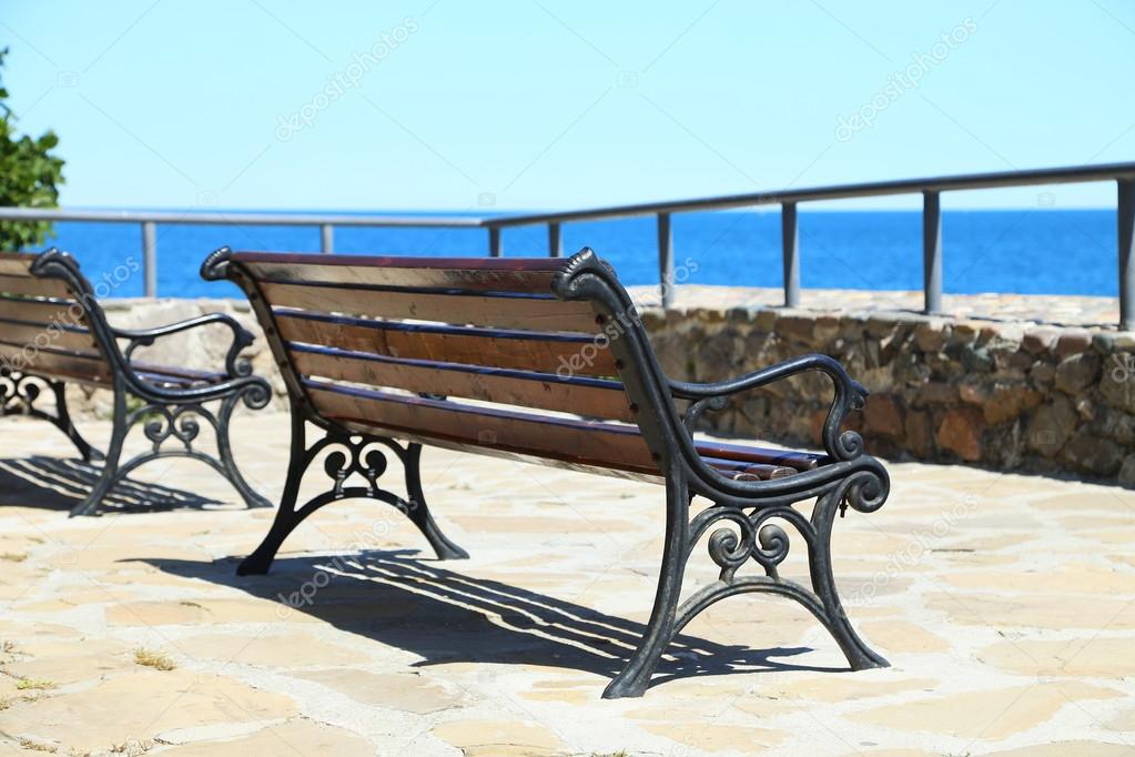 Wrought-iron bench on a stone seafront.
