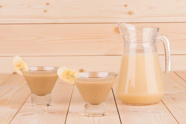 Pitcher full of banana smoothie on wood table. — Stock Photo, Image