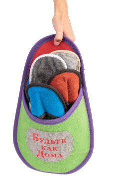 Dört terlik büyük bir ev terliğinde. Terliğin Rusça bir yazısı var. Kendini evinde gibi hisset. Beyaz arka planda izole edilmiş. Yakın plan. Bir insan eli var..