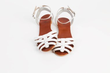 Alçak topuklu beyaz deri kadın sandaletleri. Beyaz bir yüzey üzerinde yer alır. Yakın plan..