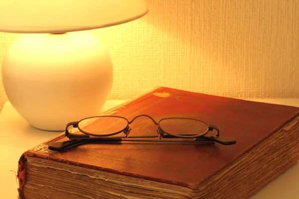 Glasses on an old book by the light of a nightlight — Stock Photo, Image