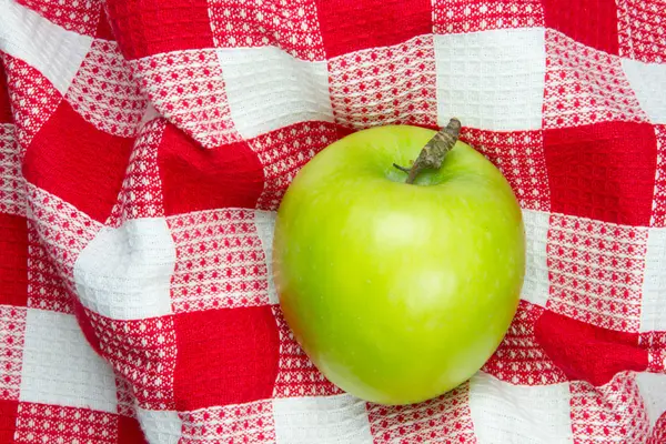 Red and white checkered table cloth with green apple — Stock Photo, Image