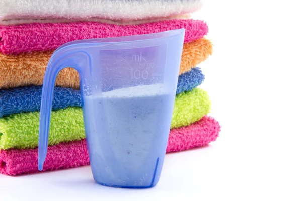 Measuring cup filled with soap flakes and piled towels — Stock Photo, Image