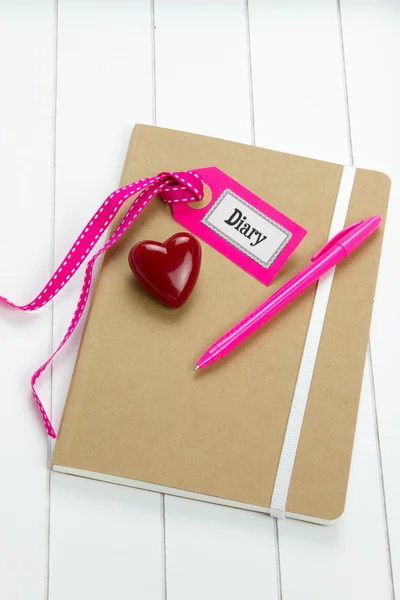 Top-view of diary with pink pen, heart symbol and label tag — Stock Photo, Image