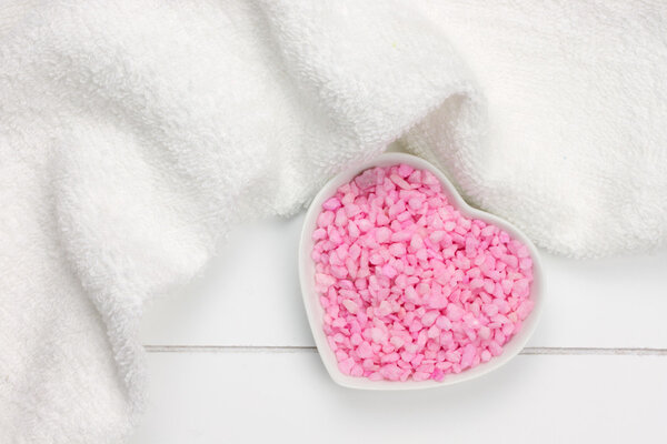 pink bath salt in heart shaped bowl and white towel on wooden su