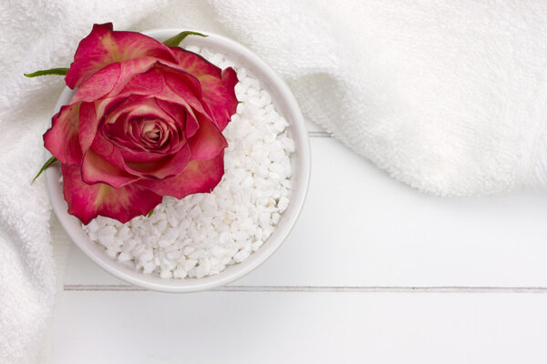 white bowl with bath salt and red rose on top of it