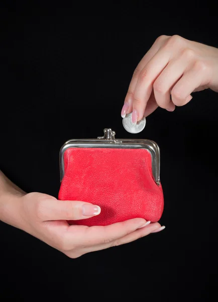 Hand throwing coin in purse on black background — Stock Photo, Image
