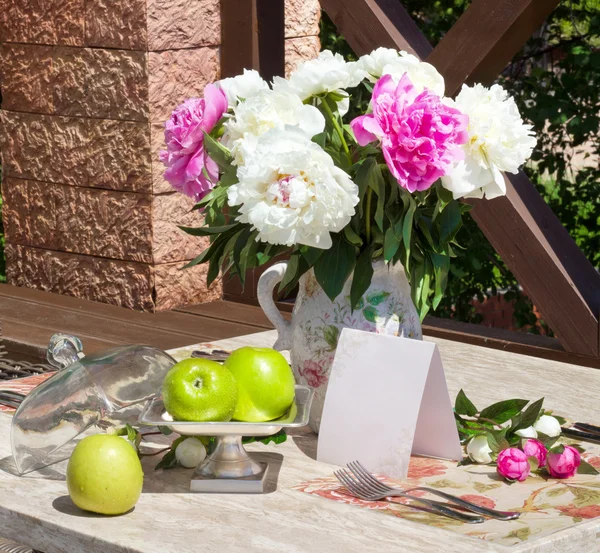 Green apples and vase of beautiful peony flowers on table. Sunny — Stock Photo, Image