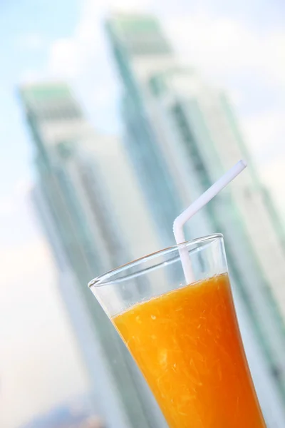 Copo cheio de suco de laranja no fundo dos arranha-céus — Fotografia de Stock