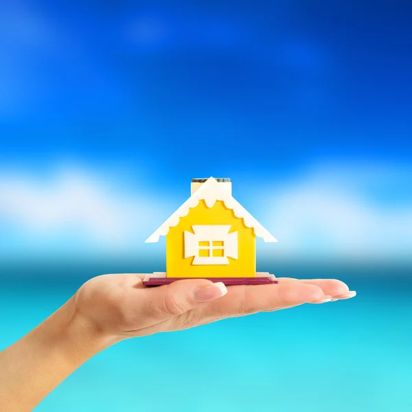 Female hand holding a yellow house on sea background — Stock Photo, Image