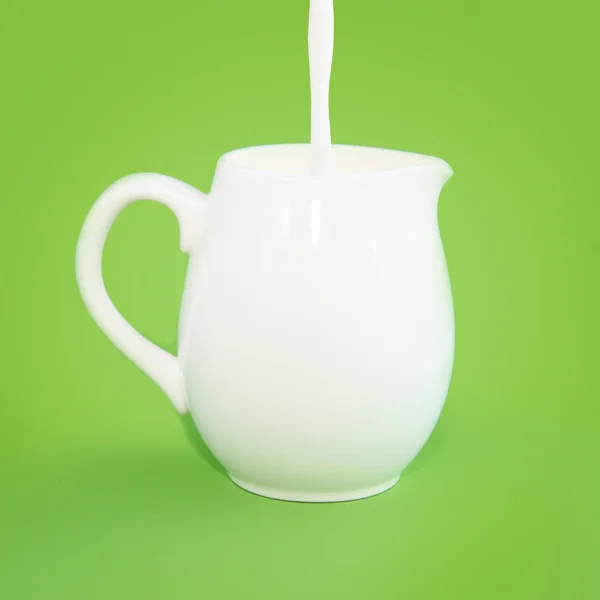 Derramando leite em um jarro branco em um fundo verde — Fotografia de Stock