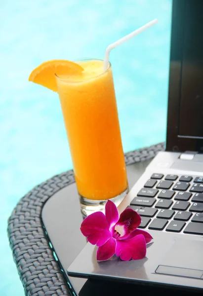 Portátil negro y jugo de naranja junto a la piscina —  Fotos de Stock