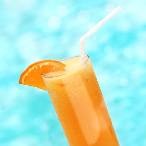 Teli pohár narancslé és egy szelet narancs, háttérben a kék víz — Stock Fotó