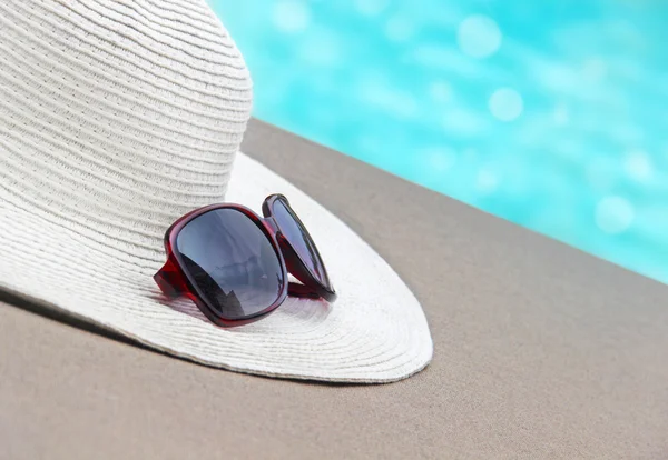 Straw hat, glasses  by the pool — Stock Photo, Image