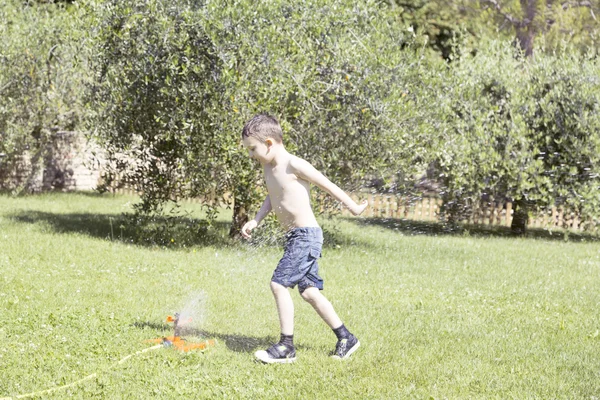 Glückliches Kind spielt mit Wasser im Garten. — Stockfoto