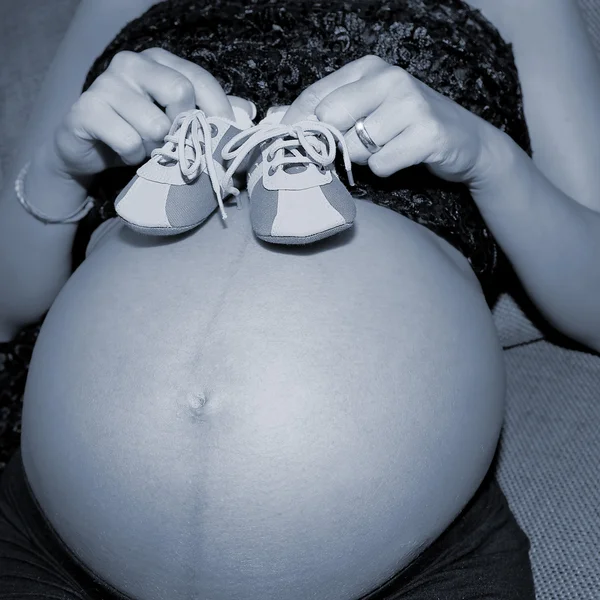 Zwangere vrouw toont haar buik met baby's schoenen — Stockfoto