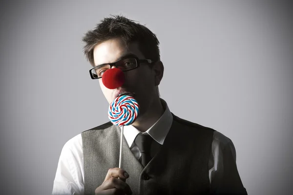 Divertente ritratto di giovane uomo alla moda con naso clown mangiare lolli — Foto Stock
